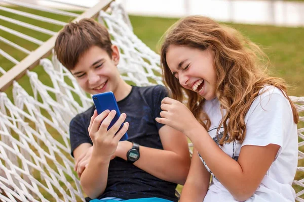 Couple of young happy teenagers. A girl and a guy laugh and watch a video together on a smartphone