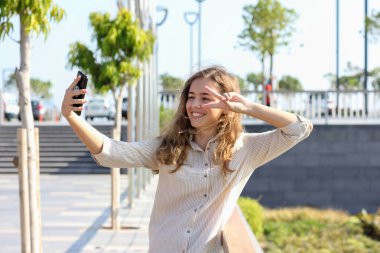 Güneşli bir günde gezinti güvertesinde selfie çeken güzel bir genç kız. Elinde telefonla gülümseyen mutlu bir genç kız.