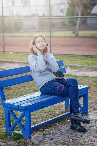 Jong mooi modieus tiener meisje luistert naar muziek op de hoofdtelefoon van een smartphone — Stockfoto