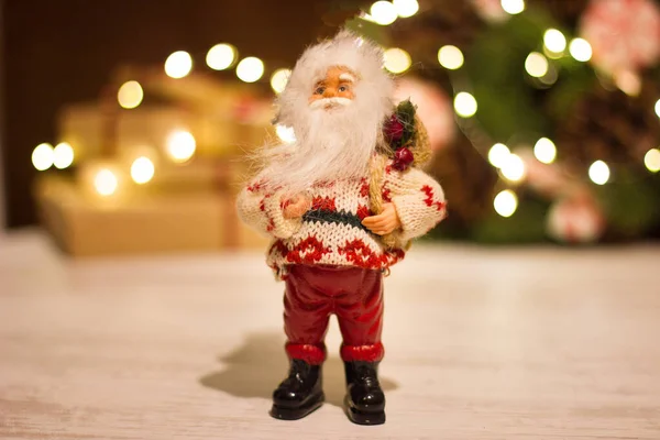 Игрушечный Санта-Клаус на фоне подарочных коробок и рождественского венка со светящейся гирляндой . — стоковое фото