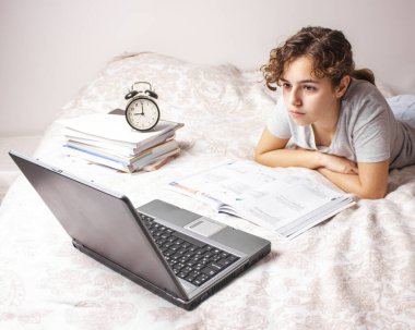 Karantinadaki genç kız yatağında internetten ders çalışıyor. Evde eğitim