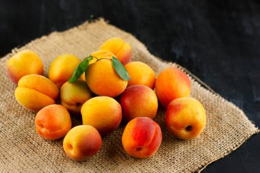 Siyah ahşap masadaki çuval bezin üzerinde taze kayısı. Olgun tatlı böğürtlenler su damlacıklarında