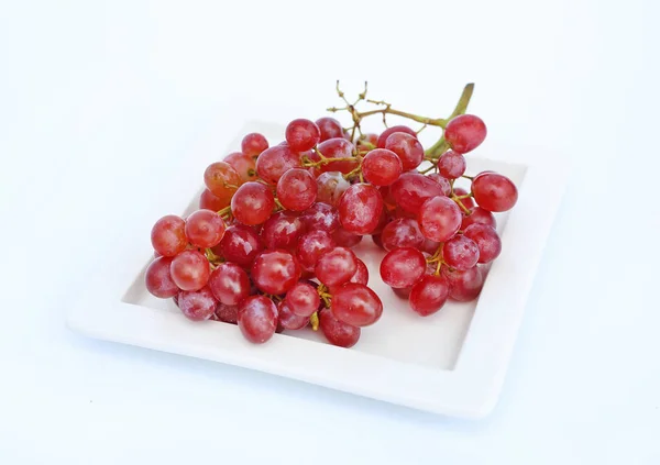 Rode druiven bessen in de witte plaat tegen de witte achtergrond — Stockfoto