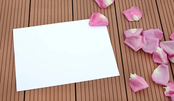 Порожня порожня картка з пелюсткою троянди на дерев'яному фоні . — стокове фото