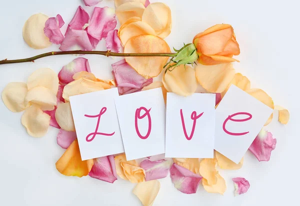 Notepaper y palabra "LOVE" con flor de rosa y pétalos sobre fondo blanco . — Foto de Stock