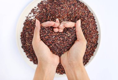 Beyaz arka plan üzerinde beyaz tabakta aşkın şeklinde kırmızı pirinç yasemin tutan el