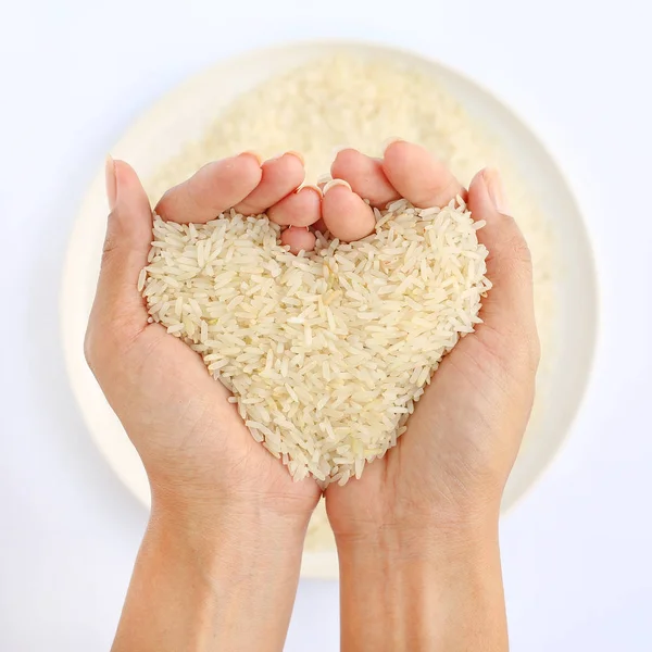 Mão segurando arroz branco Jasmim em forma de amor na placa branca contra fundo branco — Fotografia de Stock