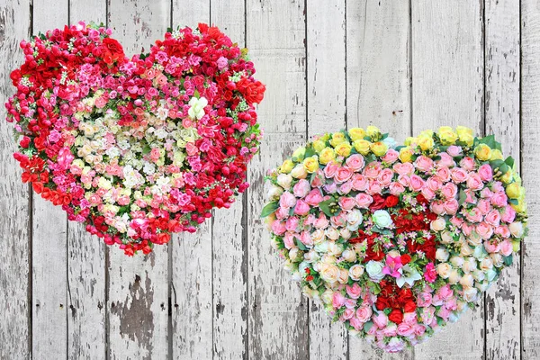 Dois corações feitos de flores de rosas no fundo da prancha de madeira . — Fotografia de Stock