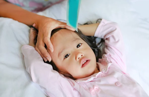 Ziek meisje liggend in bed met hand van moeder touch hoofd van haar dochter om temperatuur te controleren. — Stockfoto