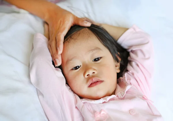 Gadis sakit berbaring di tempat tidur dengan tangan ibu menyentuh kepala putrinya untuk memeriksa suhu . — Stok Foto