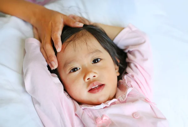 Gadis sakit berbaring di tempat tidur dengan tangan ibu menyentuh kepala putrinya untuk memeriksa suhu . — Stok Foto