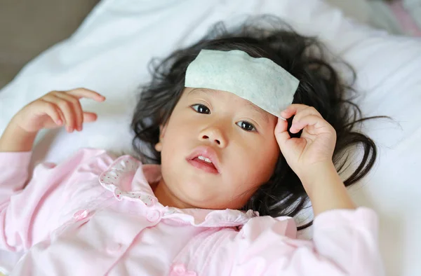 Niña enferma acostada en la cama con una gelatina fría en la cabeza . — Foto de Stock