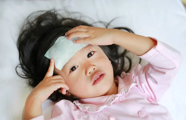 Niña enferma acostada en la cama con una gelatina fría en la cabeza . —  Fotos de Stock