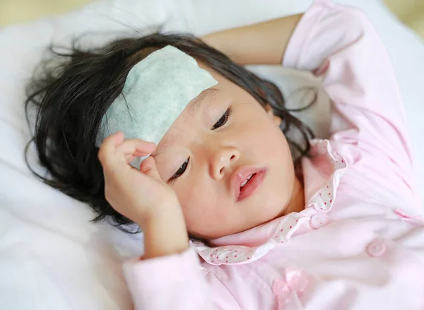 Niña enferma acostada en la cama con una gelatina fría en la cabeza . — Foto de Stock