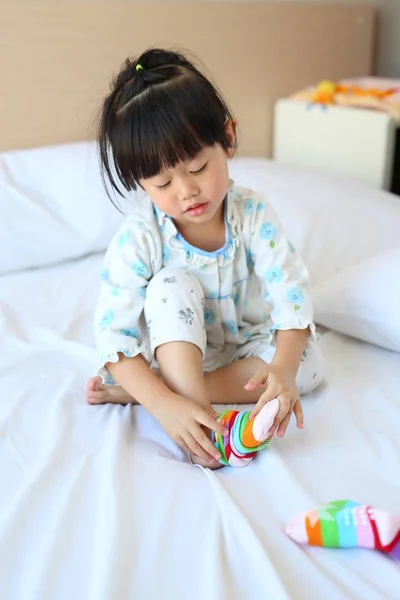 Adorable niñita tratando de poner un calcetines en la cama . — Foto de Stock