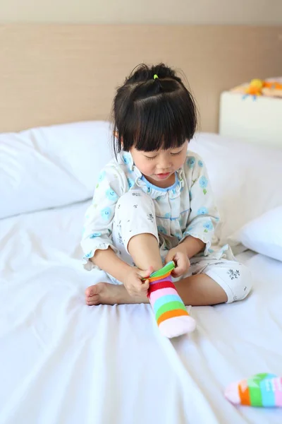 Schattig klein meisje probeert te zetten een sokken op het bed. — Stockfoto