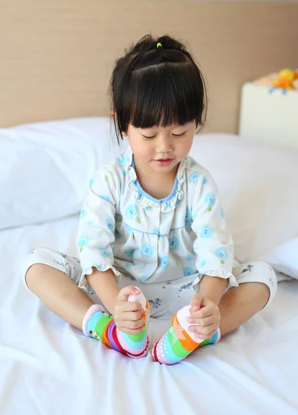 Adorable niñita tratando de poner un calcetines en la cama . — Foto de Stock