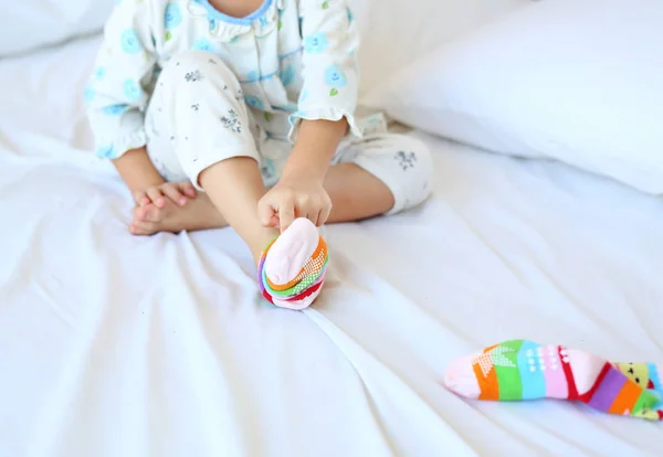 Очаровательная маленькая девочка пытается положить носки на кровать . — стоковое фото