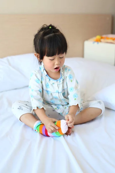 Adorable niñita tratando de poner un calcetines en la cama . — Foto de Stock