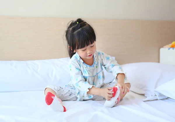 Schattig klein meisje probeert te zetten een sokken op het bed. — Stockfoto