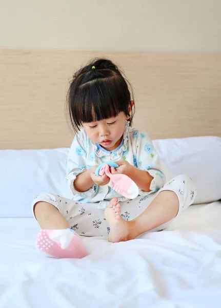 Adorable niñita tratando de poner un calcetines en la cama . — Foto de Stock