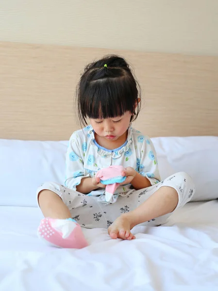 Adorable niñita tratando de poner un calcetines en la cama . — Foto de Stock