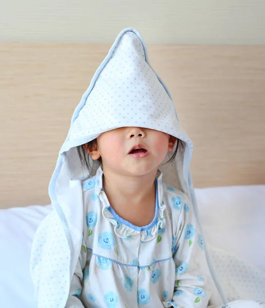 Funny little girl with blanket cover on head lying on the bed.