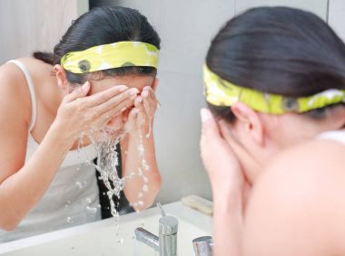 Woman applying foam cream to face reflect with bathroom mirror. clipart
