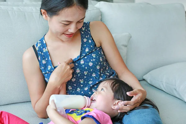 Ibu memeluknya usia anak perempuan Asia yang lucu sekitar satu tahun dan sembilan bulan minum dari botol di sofa . — Stok Foto