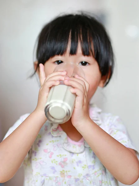 Ładna dziewczynka w piżamy, picie mleka z szkła kryty o poranku. — Zdjęcie stockowe