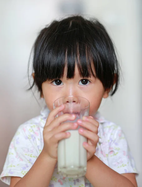 Cute Little girl in pajamas drinking milk from glass indoor at the morning. — Stock Photo, Image