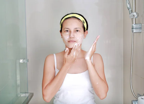 Mujer aplicando crema de espuma a la cara en el baño — Foto de Stock