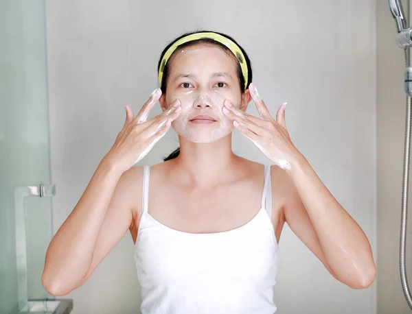 Mulher aplicando creme de espuma no rosto no banheiro — Fotografia de Stock