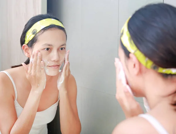Kvinna Applicera skum kräm till ansiktet avspeglar med badrumsspegel. — Stockfoto