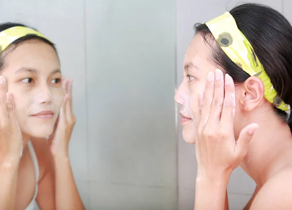 Vrouw toepassen schuim crème aan gezicht geven met badkamerspiegel. — Stockfoto