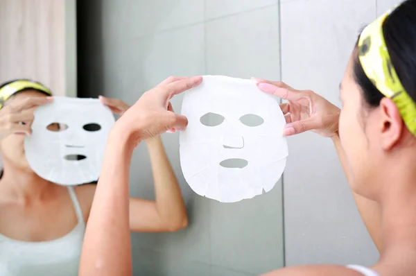 Молодая женщина наносит косметическую маску для лица в ванной комнате . — стоковое фото
