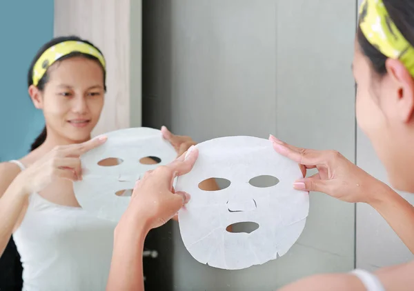 Mujer joven aplicando mascarilla facial cosmética en el baño . —  Fotos de Stock