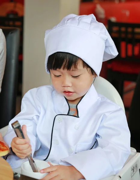 Малышка в костюме маленького шеф-повара делают мини-пиццу, готовят детскую концепцию . — стоковое фото