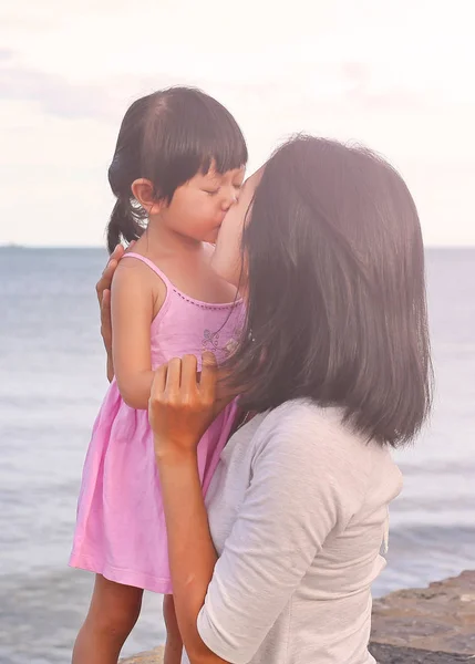 Happy family, mother and kid girl kissing with natural emotion smiling on sea background in the evening