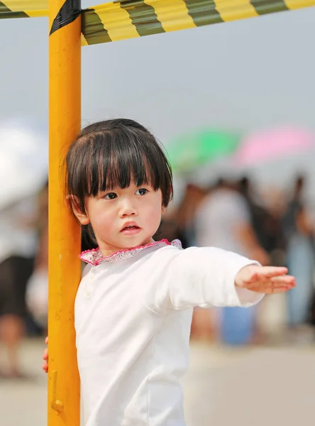 Cute little girl standing and laying at yellow metal pole, close-up outdoor portrait. — Stock Photo, Image