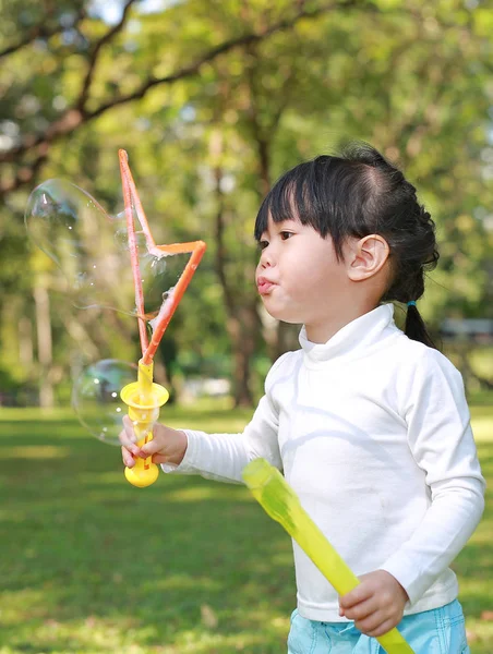 Asiatique petite fille soufflant bulles de savon dans le parc vert — Photo