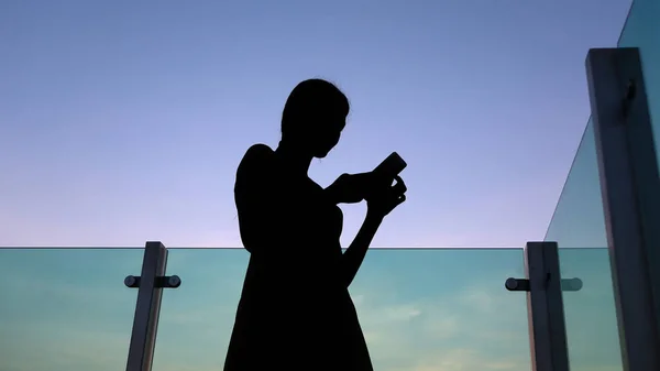 Sziluettjét nő használ smartphone, napnyugtakor a tetőn, az épület — Stock Fotó