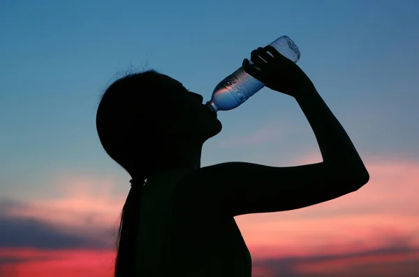 Siluet wanita Rehidrasi dan menyegarkan saat matahari terbenam — Stok Foto