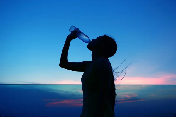 Silhueta da mulher Reidratar e refrescar ao pôr do sol — Fotografia de Stock