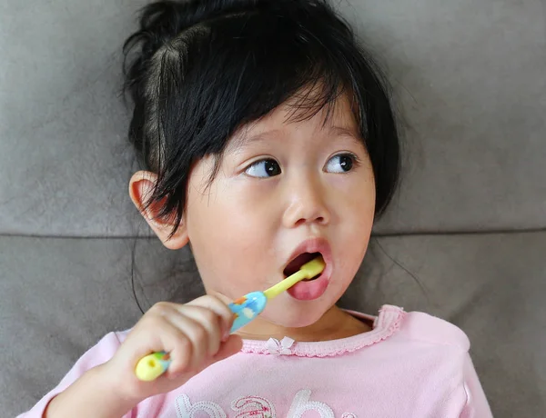 Klein meisje in roze op sofa tandenpoetsen — Stockfoto