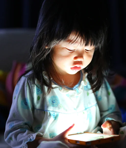 Девочка, играющая на смартфоне, лежит ночью на кровати. — стоковое фото