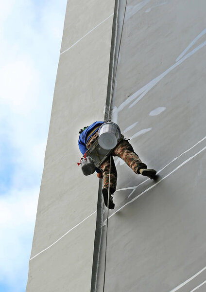 Climber worker hanging on ropes to repair building service on high rise building.