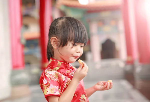Cute asian dziecko dziewczynka w języku chińskim tradycyjnym sukienka jedzenie owoc pomarańczowy święte w chińskiej świątyni w bangkok Tajlandia. — Zdjęcie stockowe