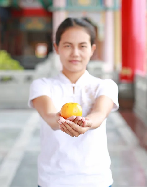 Asian woman holding sacred orange at chinese temple in bangkok, Thailand. Chinese new year concept. Focus at Orange.