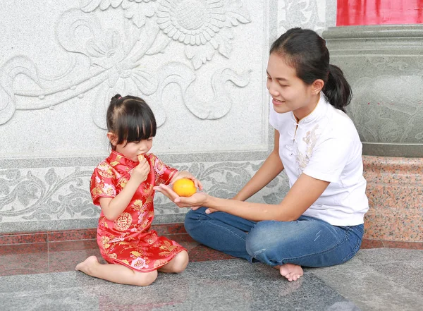 Matka i dziewczyna Cute asian dziecko w języku chińskim tradycyjnym sukienka jedzenie owoc pomarańczowy święte w chińskiej świątyni w bangkok Tajlandia. — Zdjęcie stockowe